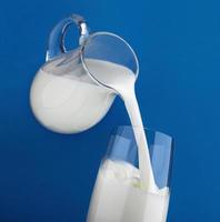 Pouring milk in glass isolated on blue background photo