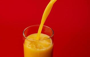 Orange juice pouring into glass isolated on red background photo