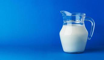 Glass jug of milk isolated on blue background with copy space photo
