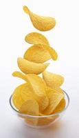 Potato chips falling into glass bowl isolated on white background photo