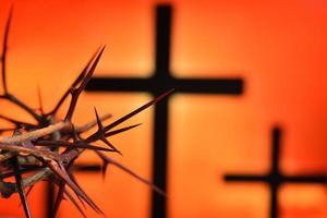 Corona de espinas de Jesucristo contra la silueta de la cruz católica al fondo del atardecer foto