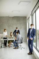 Man looking out a window and wearing a mask with a meeting in the background photo