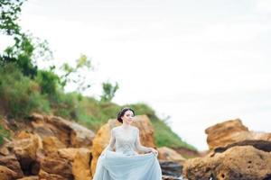 Bride in a blue light dress walking along the ocean photo