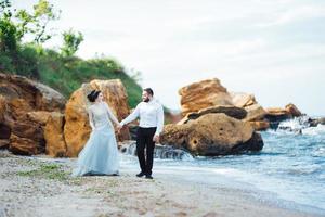 Bride in a blue dress with groom walking along the ocean shore photo