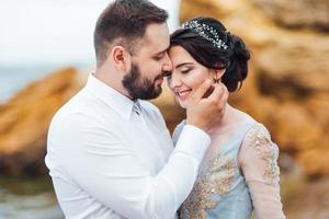 Bride in a blue dress with groom walking along the ocean shore photo