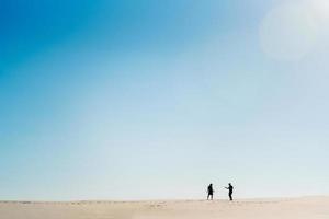 Pareja joven un chico y una chica con emociones alegres en ropa negra caminan por el desierto blanco foto