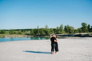 Young couple a guy with a girl in black clothes are walking on the white sand photo