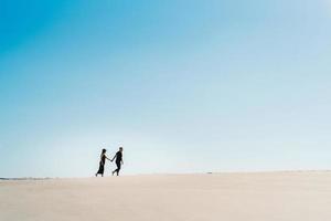 Young couple a guy and a girl with joyful emotions in black clothes walk through the white desert photo