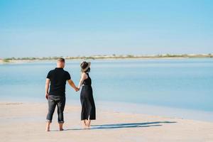 Young couple a guy with a girl in black clothes are walking on the white sand photo