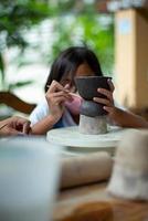 Closeup hands of little girl molding the clay on the wheel tray with blurred portrait of girl with facial mask in background photo