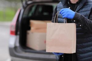 Repartidor recortada en guantes sostiene una bolsa de papel cerca del coche foto