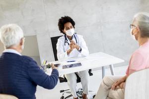 Masked mature couple talking to doctor photo