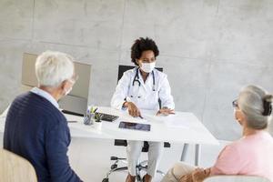 Doctor talking to mature couple wearing masks photo