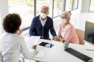 Doctor speaking to mature couple at desk with masks on photo