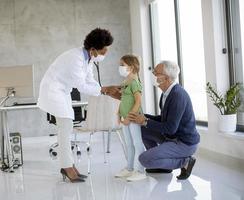 Doctor examining girl with grandparent photo