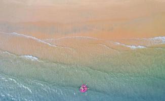 Aerial top view from drone View of boy with swim ring in the sea and shade emerald blue water and wave foam at sunrise photo