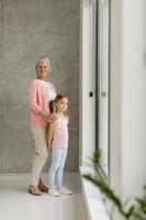 Vertical view of a grandmother and granddaughter looking out window photo