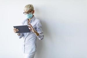 Masked mature businesswoman using a tablet