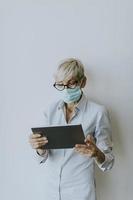 Vertical view of a masked mature businesswoman using a tablet