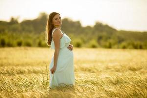 Pregnant woman in a dress in a field in bright sunlight photo