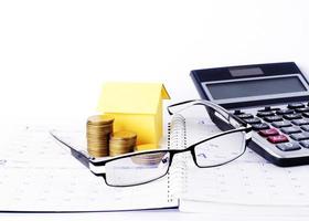 Eyeglasses and coins stack and paper house and calculator on calendar book pages for business concept photo