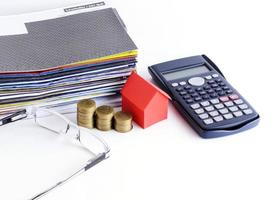 Loans concept with close up of house paper and coins stack with calculator and eyeglasses for bill payment concept photo