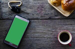 Smartphone with green screen and red coffee cup on wood background photo