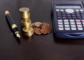 Pluma estilográfica y pila de monedas y calculadora en la mesa de madera para el concepto de finanzas foto