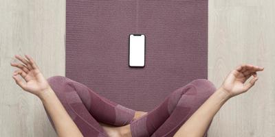 Vista superior de la mujer meditando con pantalla en blanco de smartphone