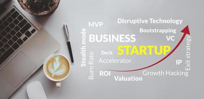 Business startup concept with keywords. Computer laptop, coffee cup, and pen on background top view. photo