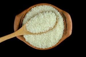 Jasmine rice in a clay pot and a wooden ladle isolated on black background