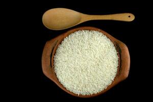 Jasmine rice in a clay pot and a wood ladle isolated on a black background photo