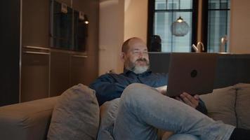 Mann, der Laptop betrachtet, der auf Couch sitzt video