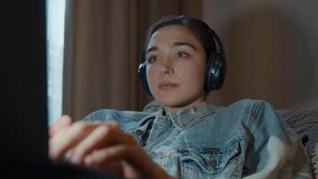 Woman on couch with headphone watching laptop video