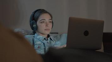 kvinna på soffan med hörlurar som håller ögonen på bärbara datorn