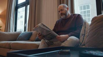 Man reading newspaper on sofa answers phone video