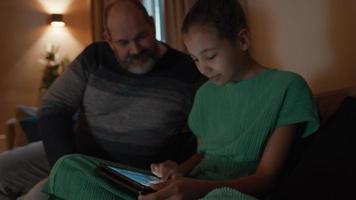 Man sitting on couch next to girl watching tablet video