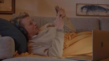 mujer, acostado, en, sofá, con, auriculares, y, smartphone video