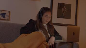 kvinna på soffan med hörlurar som håller ögonen på bärbara datorn video