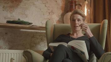 Frau, die Kaffee im Sessel mit Buch auf Schoß trinkt video