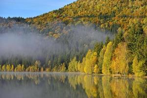 Paisaje de otoño en las montañas con árboles reflejándose en el agua en el lago de Santa Ana, Rumania