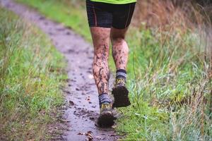 Atleta corredor en pista forestal bajo la lluvia con piernas embarradas foto