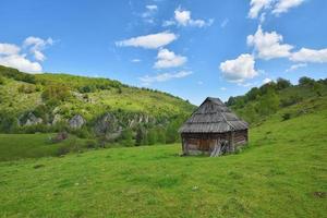 Lonely old wood house on a mountain hill with green grass against blue sky photo