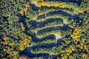 Vista aérea de una sinuosa carretera de montaña que pasa por un bosque de abetos colores otoñales foto