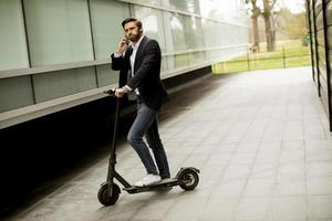 Hombre de pie sobre un scooter mientras habla por teléfono foto