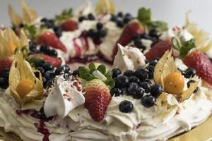 Delicioso pastel de pavlova corona de merengue francés y crema batida decorada con fresas y arándanos Physalis foto