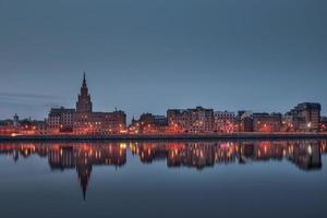 Night view on the illuminated riverside with reflection on the river in Riga photo