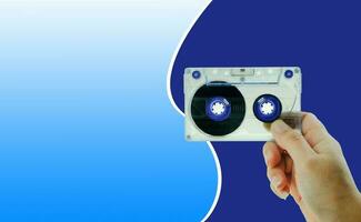 Woman's hand holding tape cassette at blue background photo