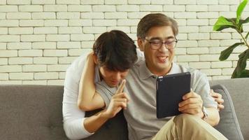 hijo asiático enseñando a su padre a usar una tableta video