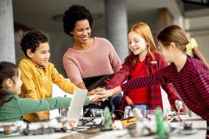 Niños felices con su profesora de ciencias afroamericana con programación de portátiles, juguetes eléctricos y robots en el aula de robótica
